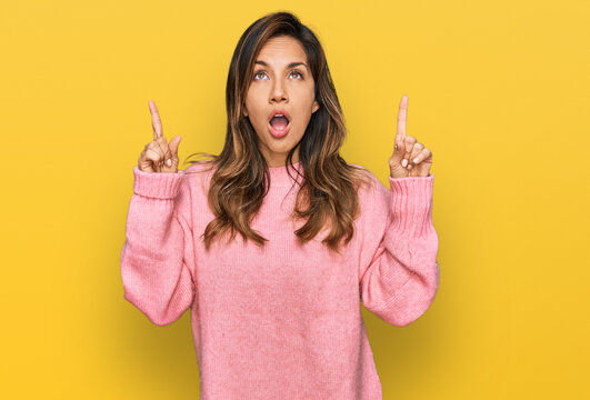 Young hispanic woman wearing casual clothes amazed and surprised looking up and pointing with fingers and raised arms.