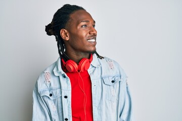 African american man with braids listening to music using headphones looking away to side with smile on face, natural expression. laughing confident.