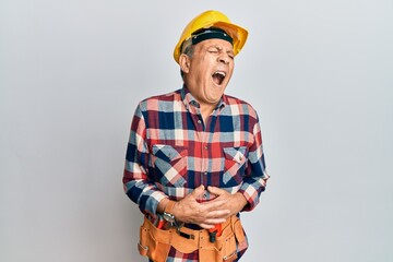 Senior hispanic man wearing handyman uniform with hand on stomach because nausea, painful disease...