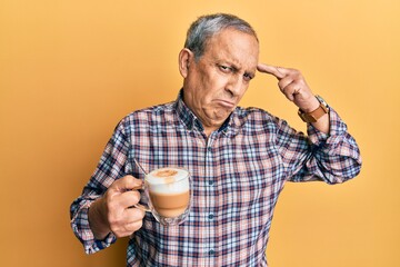 Handsome senior man with grey hair drinking a cup coffee shooting and killing oneself pointing hand and fingers to head like gun, suicide gesture.