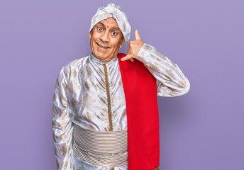 Senior hispanic man wearing tradition sherwani saree clothes smiling doing phone gesture with hand and fingers like talking on the telephone. communicating concepts.