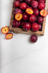 Ripe red plums in a white plate on marble background. Healthy food. 