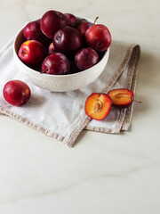 Ripe red plums in a white plate on marble background. Healthy food. 