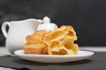 Airy profiteroles, puffs, popovers, eclaires on white plate on tea set background.