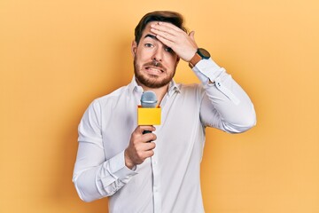 Handsome caucasian man with beard holding reporter microphone stressed and frustrated with hand on...