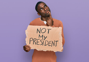 Young african american man holding not my president protest banner serious face thinking about...