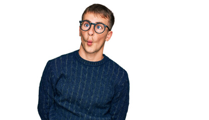Young blond man wearing casual clothes and glasses making fish face with lips, crazy and comical...