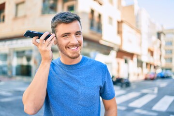 Young caucasian man smiling happy listening audio message using smartphone at the city.