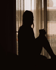 silueta de mujer frente una ventana con una taza en mano.