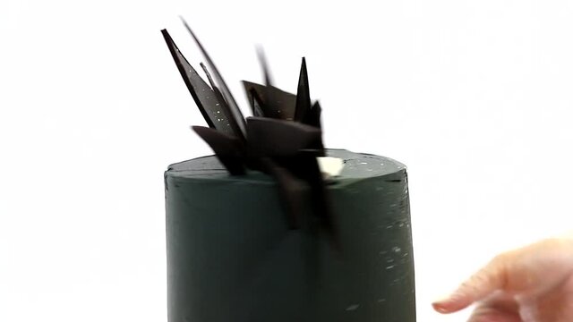 Stylish black cake with chocolates and marshmello on a white background. Pastry chef rotates the dessert on the stand. Futuristic unusual birthday cake for people with character. 