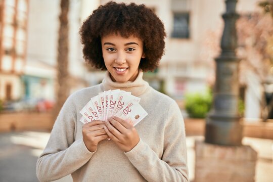 Young hispanic girl smiling happy holding israel shekels at the city.