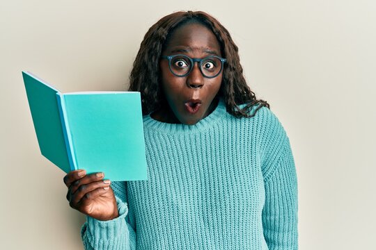 African Young Woman Reading A Book Wearing Glasses Scared And Amazed With Open Mouth For Surprise, Disbelief Face