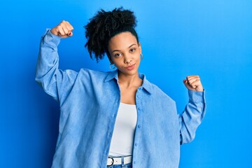 Young african american girl wearing casual clothes showing arms muscles smiling proud. fitness concept.