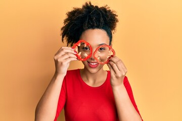 Young african american girl holding red pepper as a glasses winking looking at the camera with sexy...