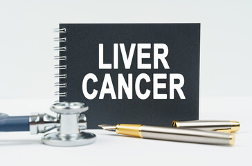 On a white background lies a stethoscope, a pen and a black notebook with the inscription - LIVER CANCER