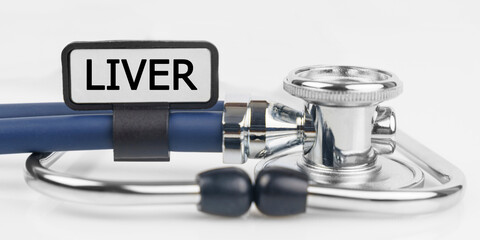 On the white surface lies a stethoscope with a plate with the inscription - LIVER