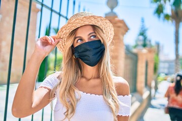 Young blonde tourist girl wearing summer style and coronavirus mask walking at the city.