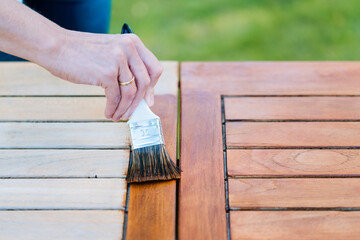 hand holding a brush applying varnish paint on a wooden garden table - painting and caring for wood with oil