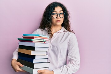 Young brunette woman with curly hair holding a pile of books skeptic and nervous, frowning upset because of problem. negative person.
