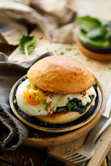 Burger with fried egg and spinach served on a plate, close up view. Vegetarian food concept