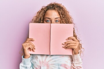 Beautiful caucasian teenager girl reading a book covering face smiling with a happy and cool smile...