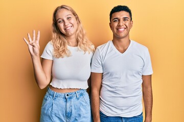 Young interracial couple wearing casual white tshirt showing and pointing up with fingers number four while smiling confident and happy.