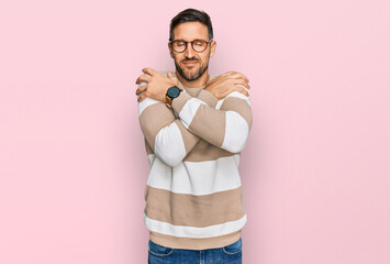 Handsome man with beard wearing casual clothes and glasses hugging oneself happy and positive, smiling confident. self love and self care