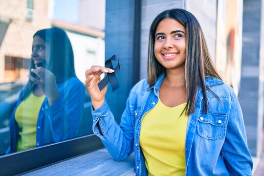 Young latin woman smiling happy holding black ribbon at city.