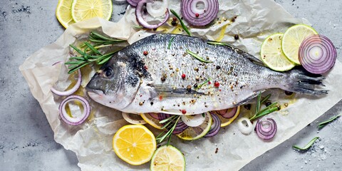 Fresh fish dorado. Raw dorado with herbs, spices and lemon and lime slices ready to cook on a gray background. Top view.  Fresh fish gilt-head bream  with salt, herbs and pepper.
