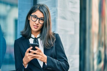 Fototapeta premium Young hispanic businesswoman smiling happy using smartphone at the city.