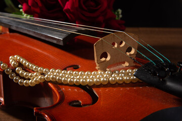 Violin and pearl necklace, arrangement with violin and pearl necklace on wooden surface, low key...
