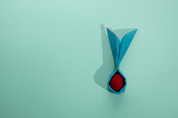 An red Easter egg in a green rabbit-shaped napkin. Flat lay on mint background.