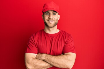Young caucasian man wearing delivery uniform and cap happy face smiling with crossed arms looking at the camera. positive person.