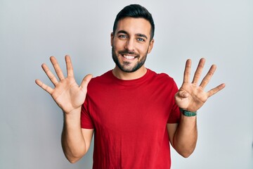 Naklejka premium Young hispanic man wearing casual clothes showing and pointing up with fingers number nine while smiling confident and happy.