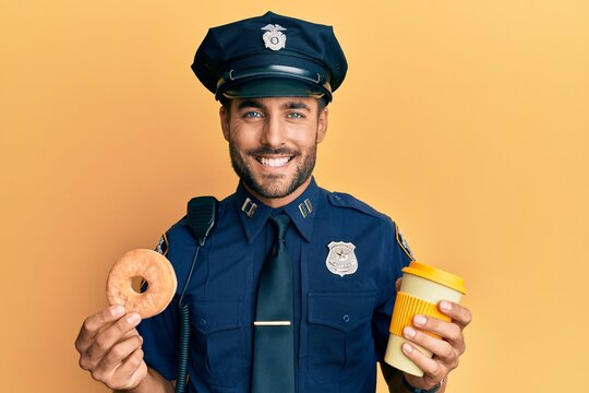 Handsome hispanic police man eating donut and drinking coffee smiling with a happy and cool smile on face. showing teeth.