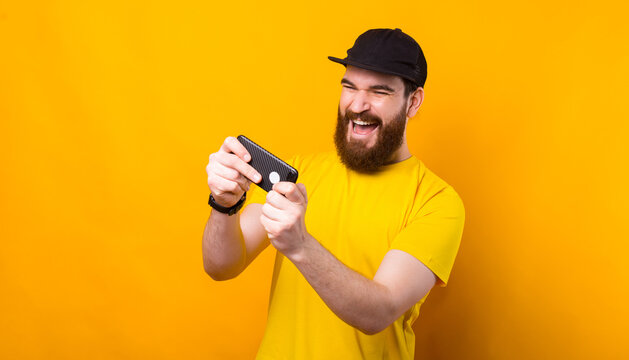 Cheerful bearded man in yellow t-shirt playing at smartphone