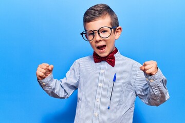 Cute blond kid wearing nerd bow tie and glasses celebrating surprised and amazed for success with...