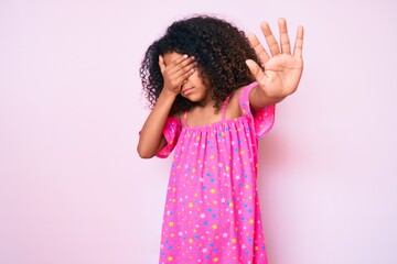 African american child with curly hair wearing casual dress covering eyes with hands and doing stop gesture with sad and fear expression. embarrassed and negative concept.