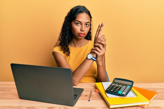 Young african american girl working at the office with laptop and calculator holding symbolic gun with hand gesture, playing killing shooting weapons, angry face
