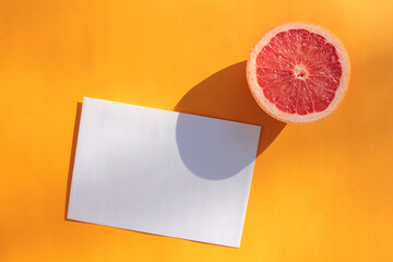 Summer still life with half of grapefruit and blank paper card on orange background. Invitation...