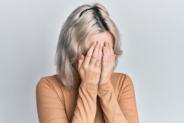 Young blonde girl wearing casual clothes with sad expression covering face with hands while crying. depression concept.