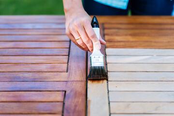 hand holding a brush applying varnish paint on a wooden table - painting and caring for wood with oil