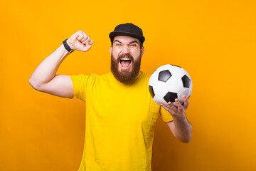 Amazed bearded hipster man celebrating victory and holding soccer ball