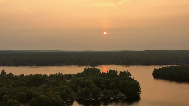 Aerial shot of houses amidst trees at lakeshore against sky, drone flying forward over lake at sunset - Berkshire County, Massachusetts