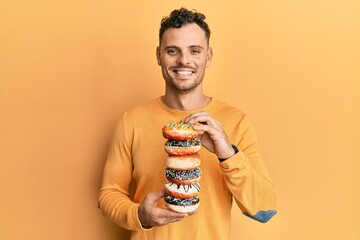 Young hispanic man holding tasty colorful doughnuts smiling with a happy and cool smile on face. showing teeth.