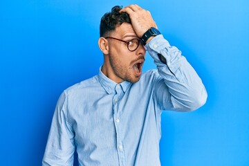 Young hispanic man wearing casual clothes and glasses surprised with hand on head for mistake, remember error. forgot, bad memory concept.