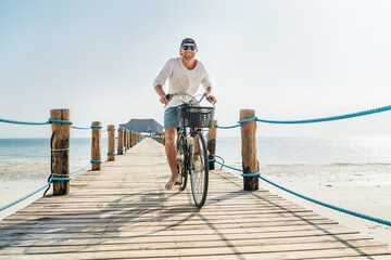 Portrait of a happy smiling man dressed in light summer clothes and sunglasses riding a bicycle on...