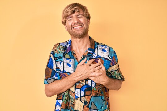 Young blond man wearing summer shirt smiling with hands on chest with closed eyes and grateful gesture on face. health concept.