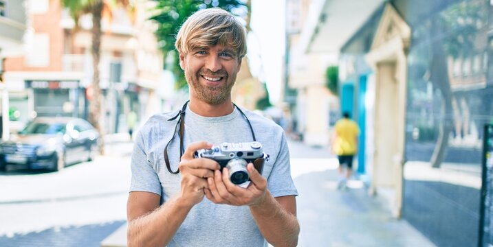 Young irish photographer man smiling happy using vintage camera at street of city.