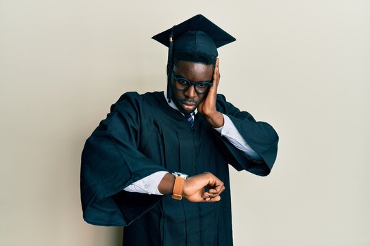 Handsome black man wearing graduation cap and ceremony robe looking at the watch time worried, afraid of getting late
